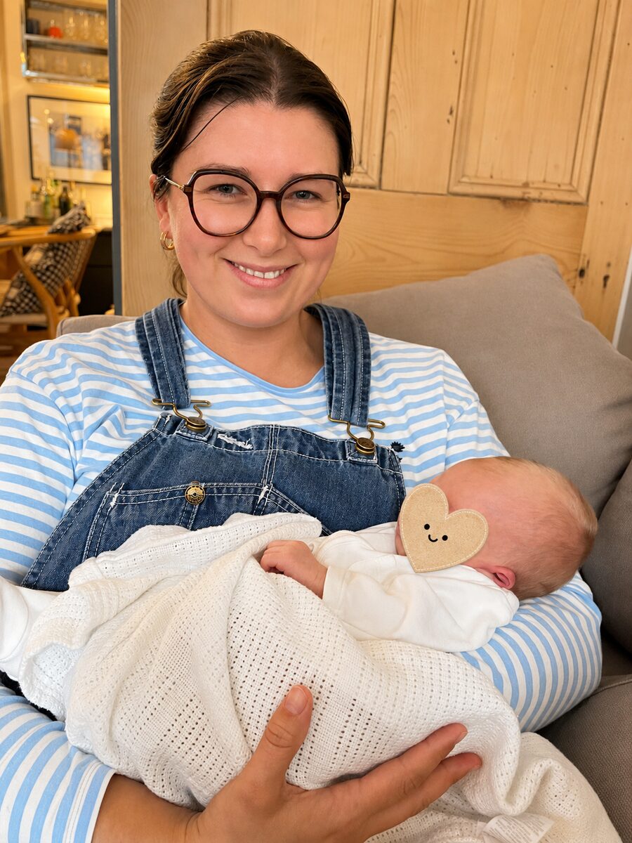 Imo Sands, doula in South East London, smiling while holding a sleeping newborn baby wrapped in a white blanket