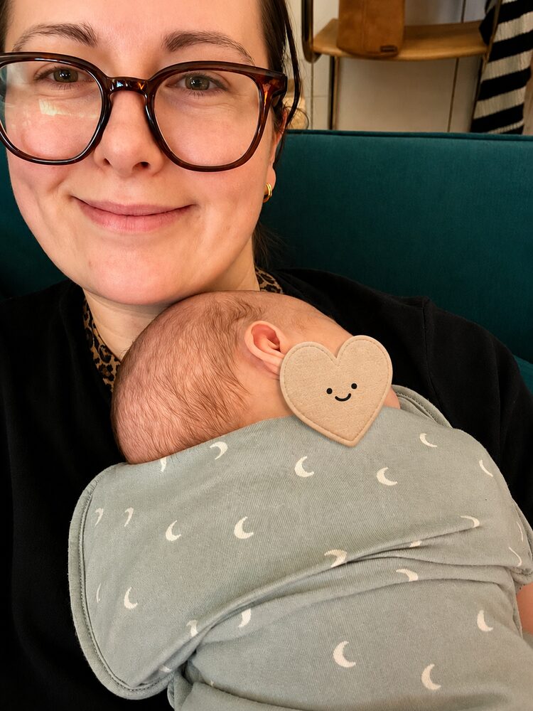 Imo Sands, doula, holding a sleeping newborn baby wrapped against her chest in a sling